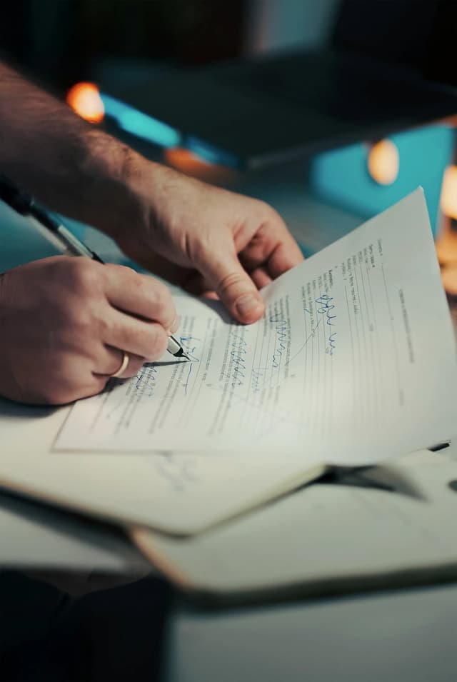 A hand signing a printed agreement with a pen