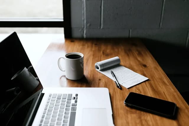 A laptop, a coffee and a notepad on a wooden desk