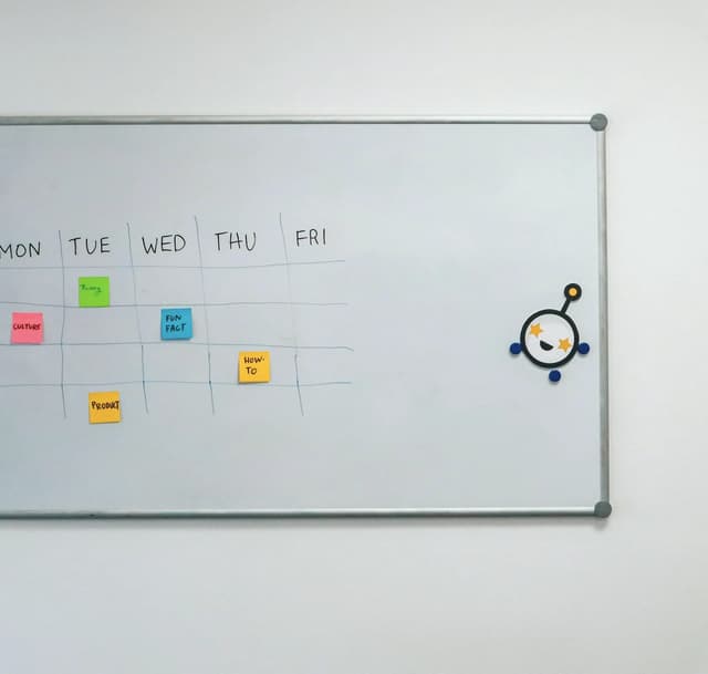 A whiteboard week planner with sticky notes under the days