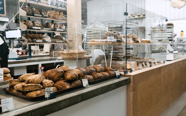 A bakery counter before opening: croissants and loaves on trays, the till screen on the left