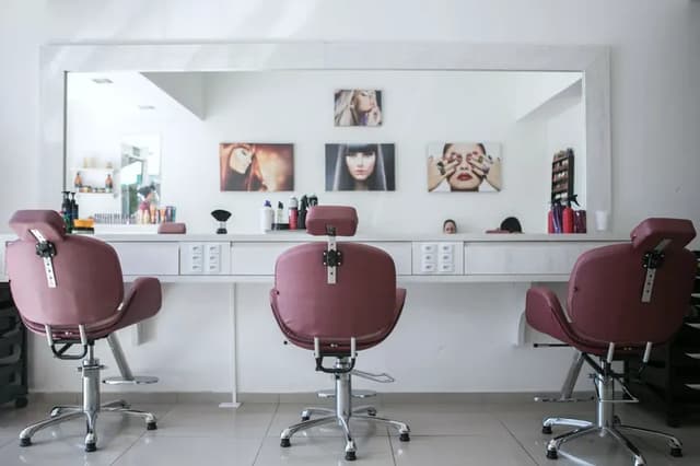 Three empty salon chairs facing a long mirror