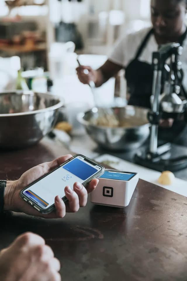 A phone held to a card reader on a kitchen counter