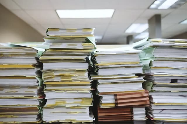 Tall stacks of paper files on an office desk
