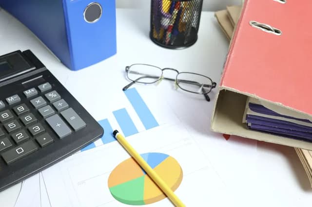 A calculator, folders and printed charts on an office desk.